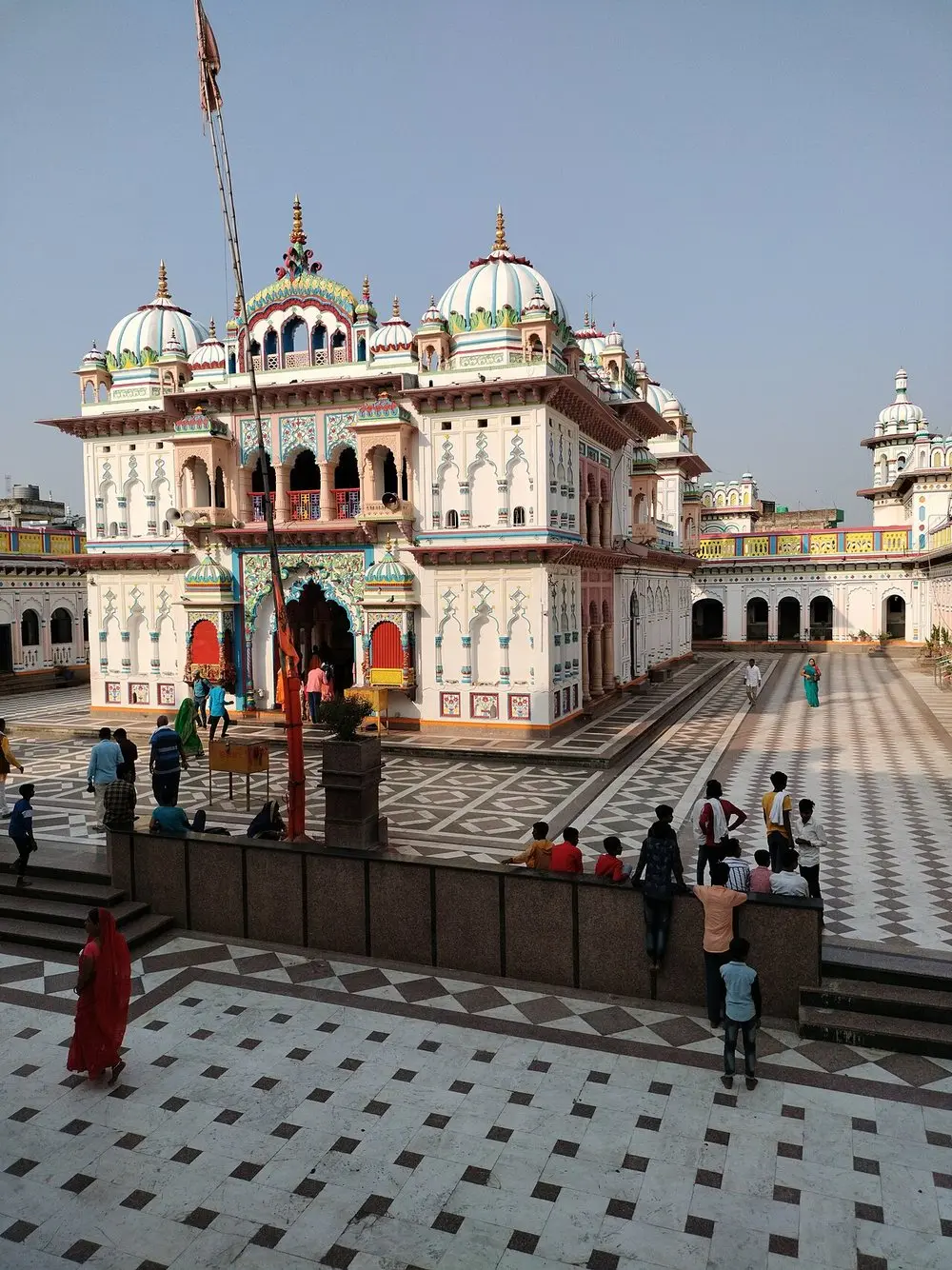 The white, domed front of the Janaki Mandir across its tiled courtyard, with visitors on the steps.